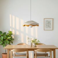 A natural linen pleated scallop lampshade with a mustard scalloped edge, hanging against a neutral background.
