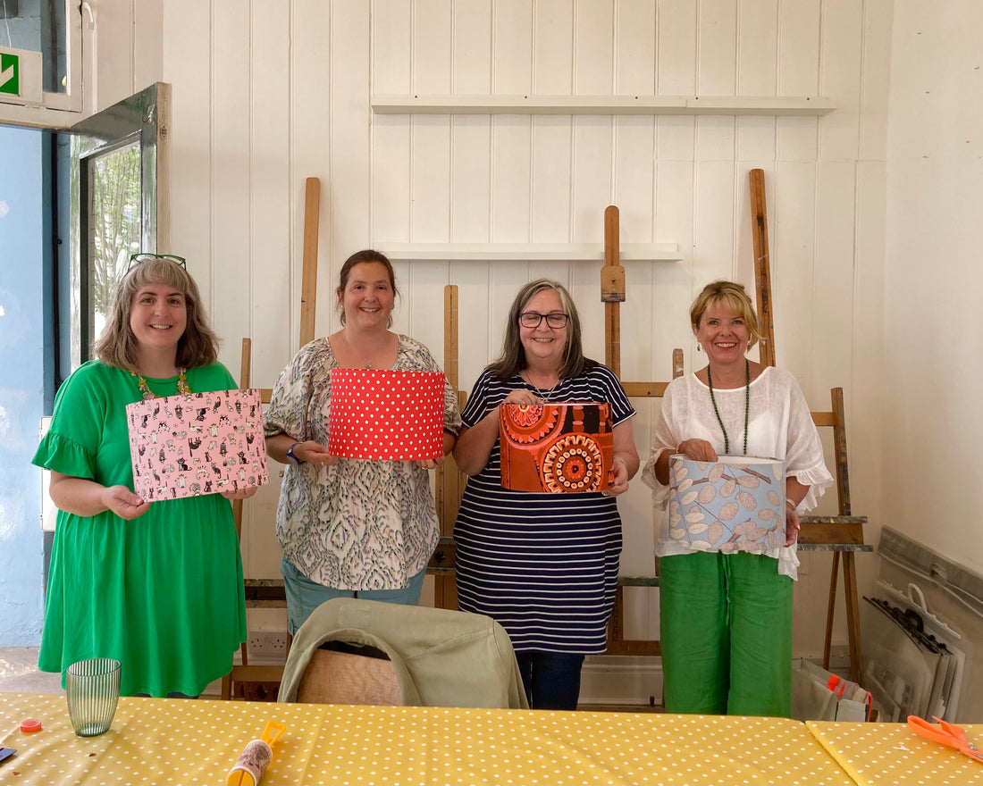 Four women holding colourful lampshades that they have just made in the workshop  