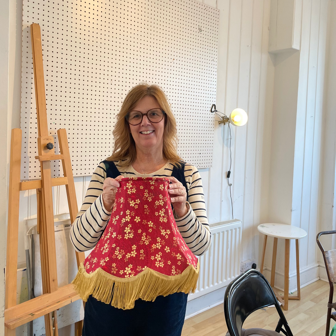 Woman holding a red floral lampshade that she has made in the workshop 