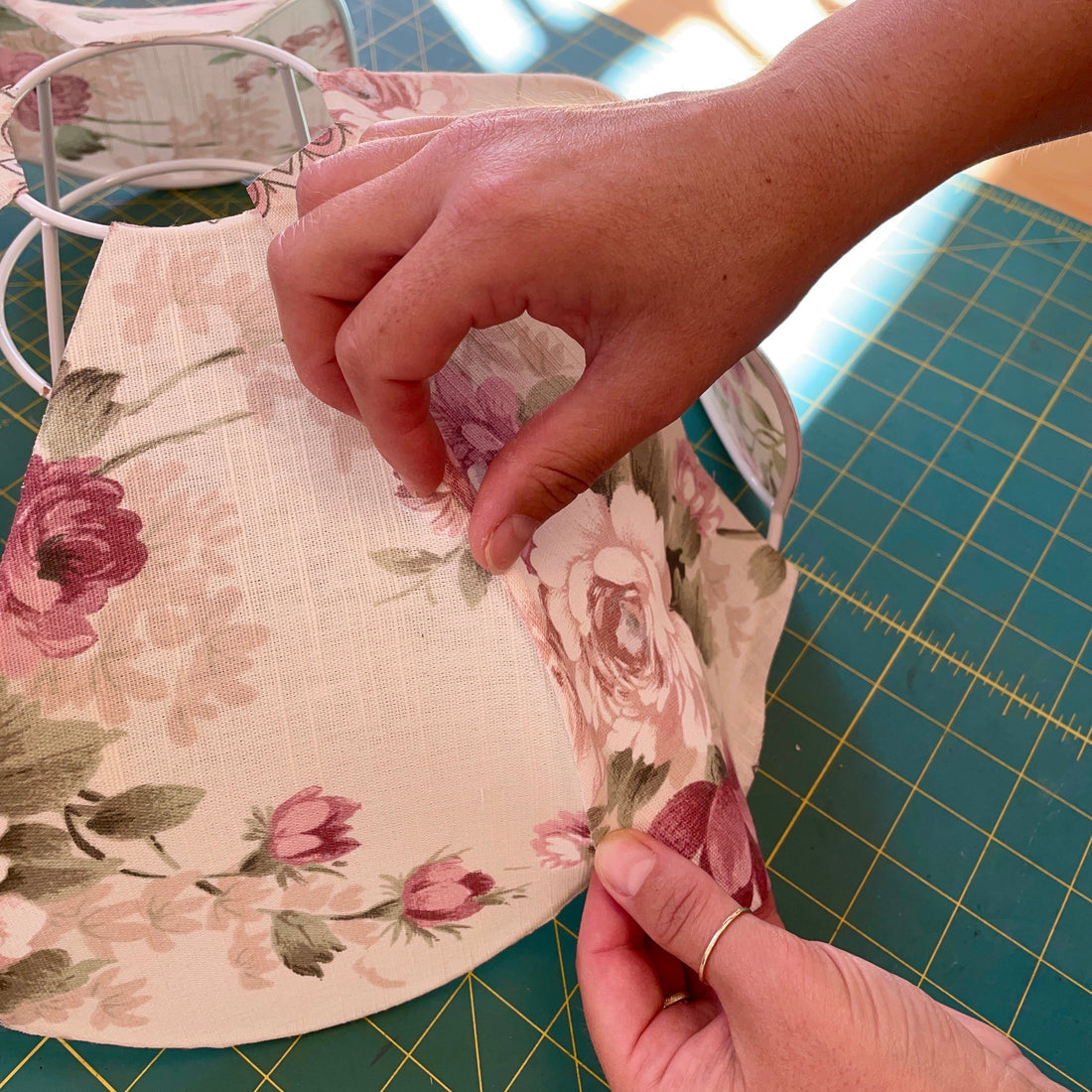 A close-up of a person's hands adjusting the vintage floral fabric on to the scallop lampshade frame