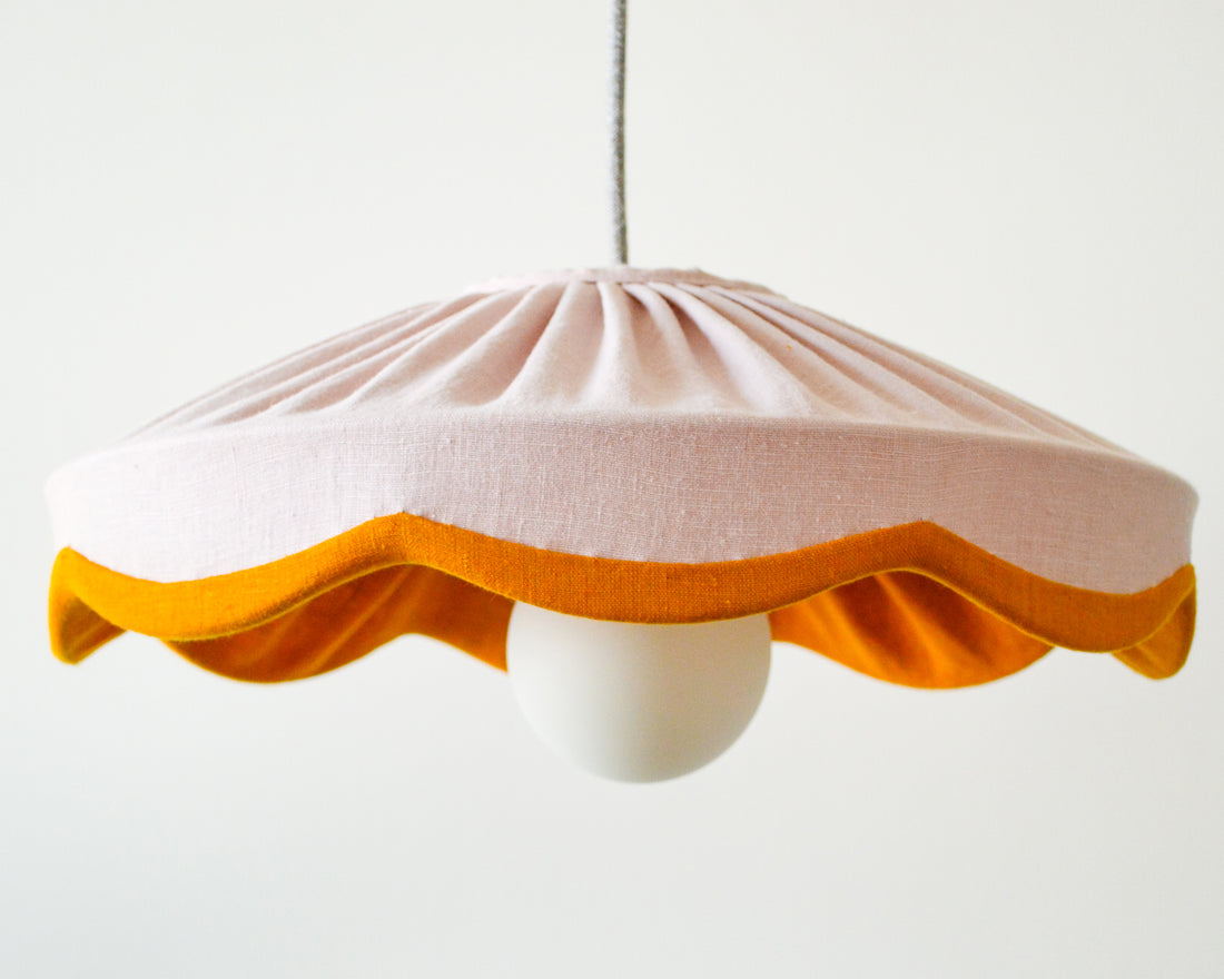 A dusty pink pleated scallop lampshade with a mustard linen edge, designed to fit a standard ceiling lamp.