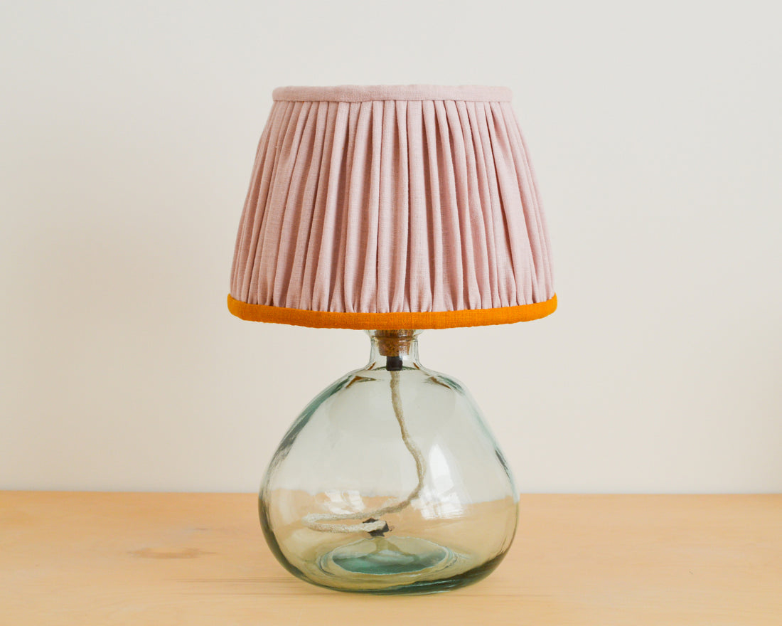 A handmade pink and mustard gathered lampshade with a french drum shape, on a glass lamp base.