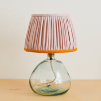 A handmade pink and mustard gathered lampshade with a french drum shape, on a glass lamp base.