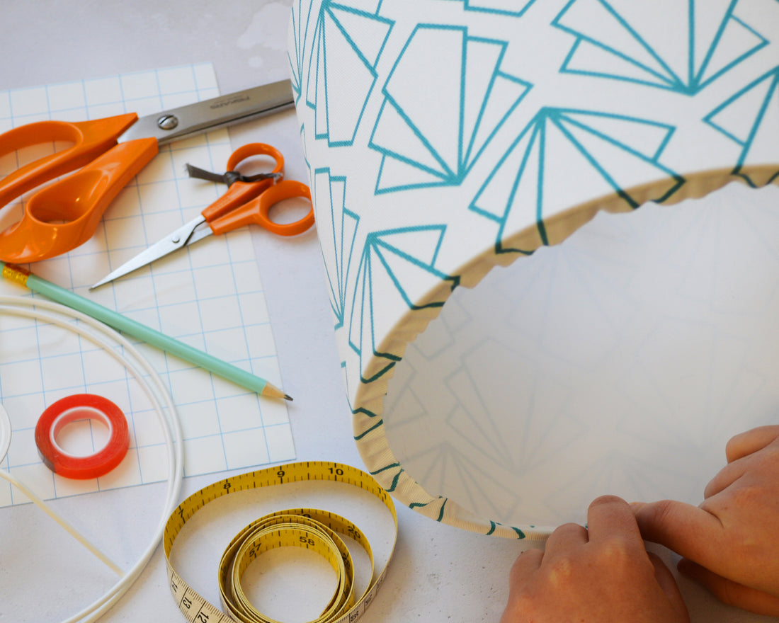 A person crafting a lampshade with geometric patterns, sitting at a table with scissors, tape measure, and other materials.